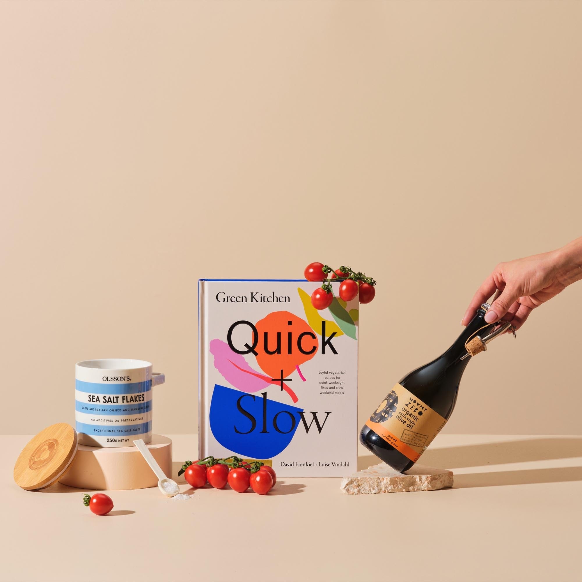  This image displays the gift bundle 'Veg Out' featuring the cover of 'Quick and Slow', Mount Zero Olive Oil, Olsson's Sea Salt Flakes - accessorised with red cherry tomatoes.