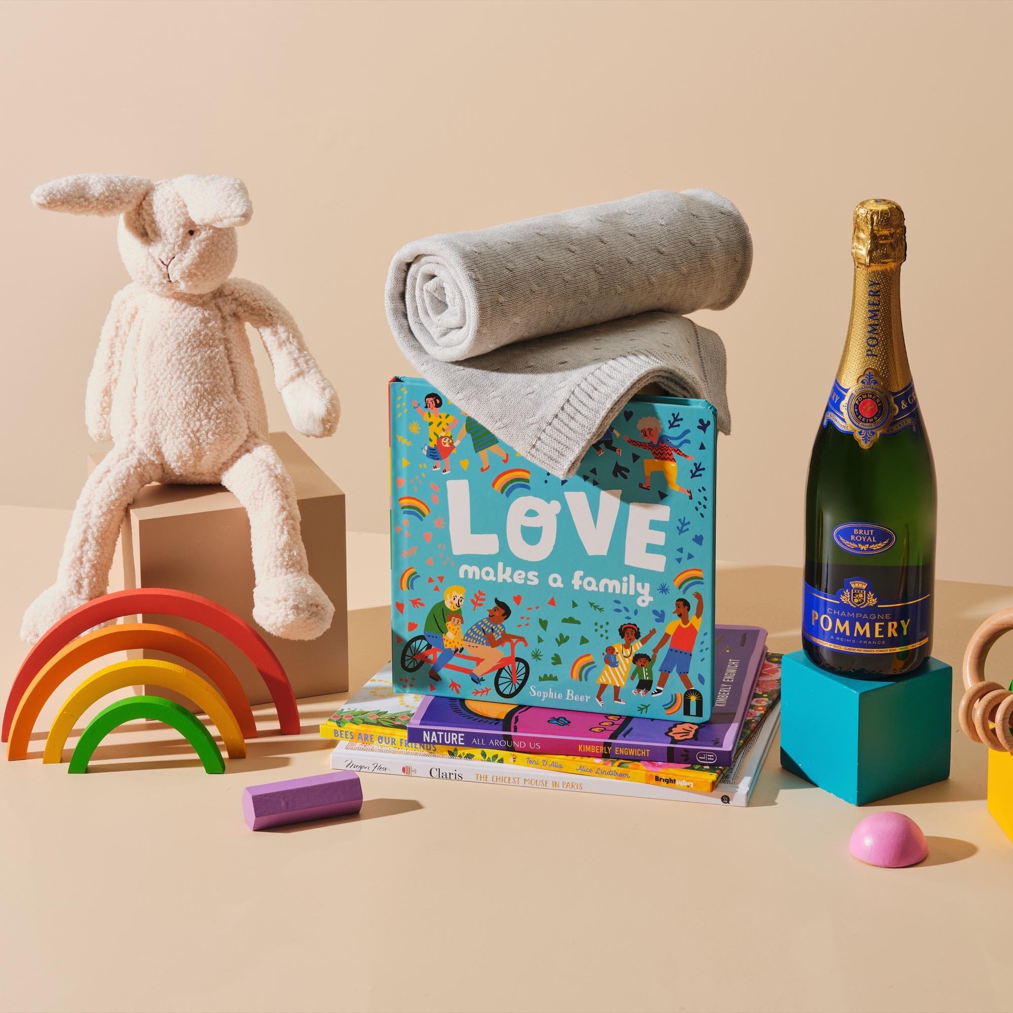 This image features Sophie Beer's Love Makes a Family placed on top of Nature All Around Us by Kimberly Engwicht, Bees Are Our Friends written by Toni D’Alia and Claris, The Chicest Mouse in Paris by Megan Hess. Also included in the image is Purebaby’s Natural Teething Ring, Essentials Blanket and Bonnie the Bunny Toy. As for something for Mum, the Champagne Pommery Brut Royal, is also featured in this image. 