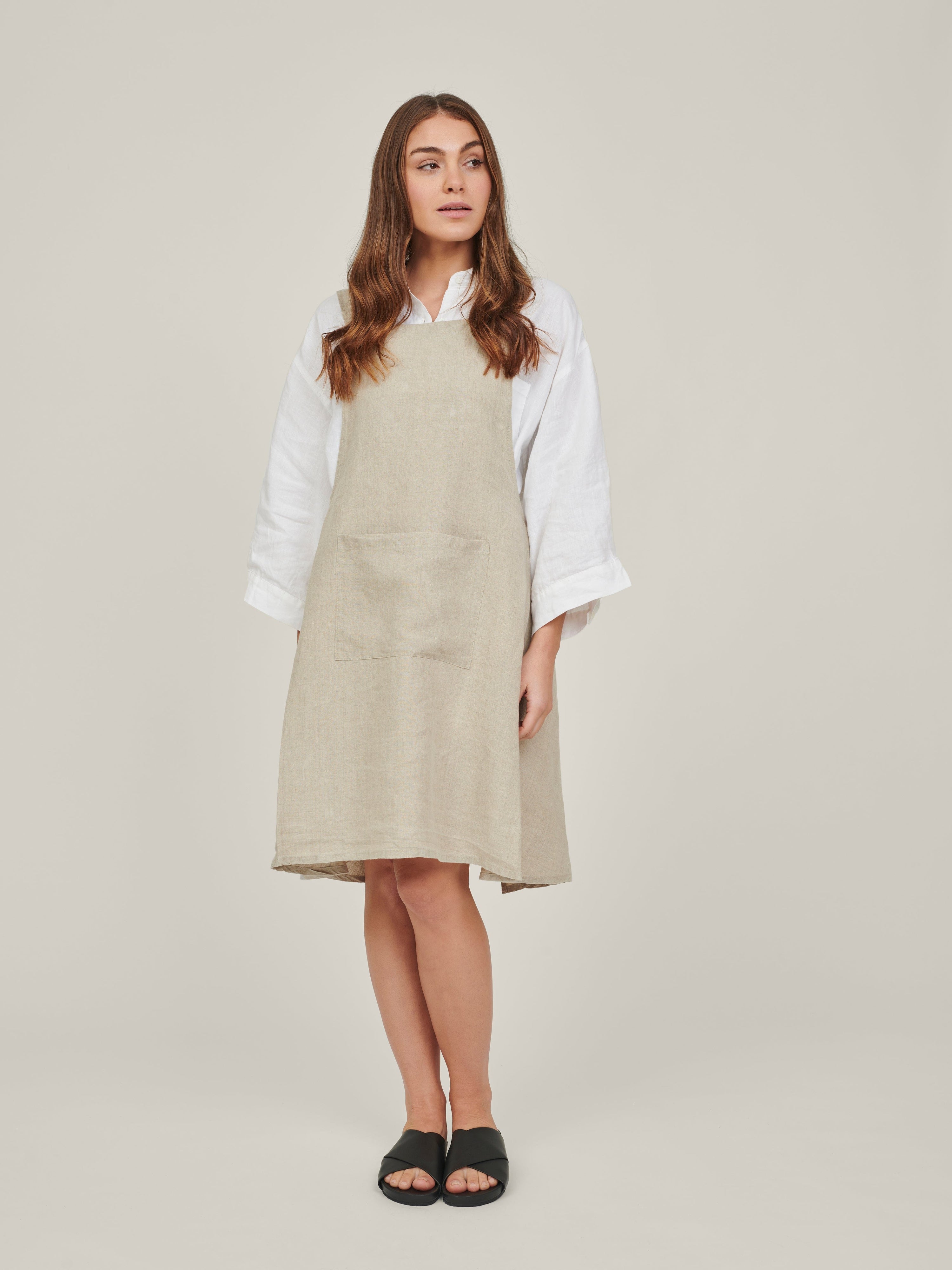 Displays Carlotte and Gee's linen apron in the colour natural, on a model 